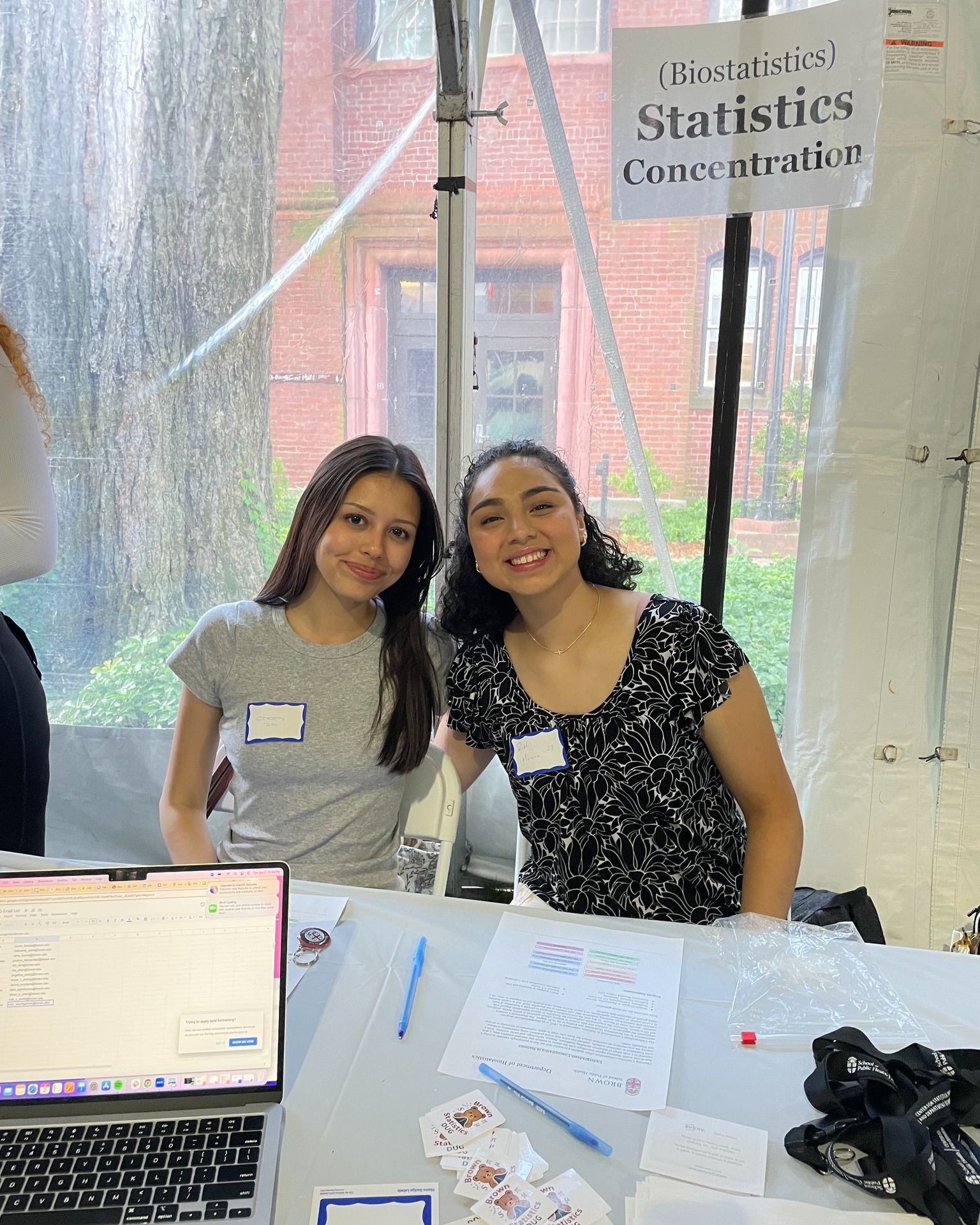 two young women smile sitting behind table