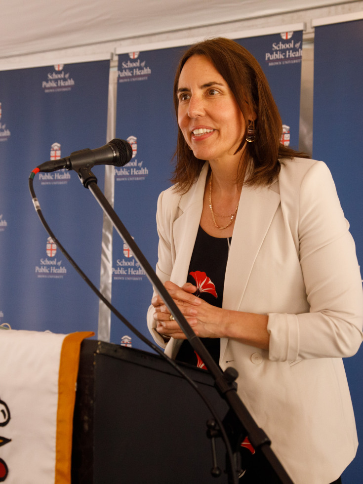 Dean Francesca Beaudoin speaks at a podium microphone before a dark blue SPH background.