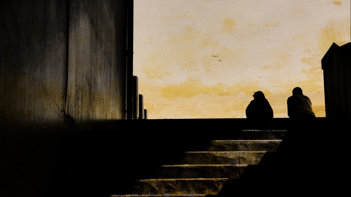 Illustration of the silhouette of two unhoused people sitting in an underpass