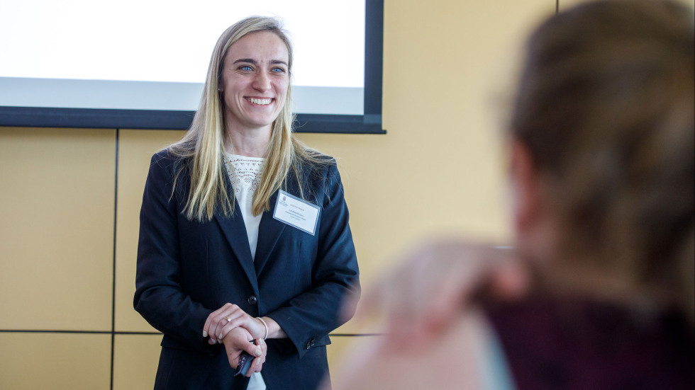 A woman in a blue blazer smiling in front of a room after presenting.